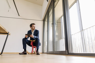 Businessman sitting on rocking horse with tablet - KNSF01155