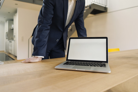 Geschäftsmann stützt sich mit Laptop auf einen Tisch, lizenzfreies Stockfoto