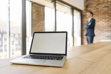 Laptop auf Tisch mit Geschäftsmann im Hintergrund - KNSF01160