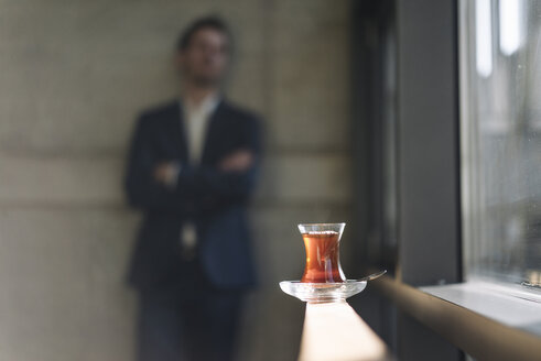 Ein Glas türkischer Tee am Fenster mit einem Geschäftsmann im Hintergrund - KNSF01179