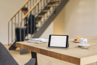 Tablet auf dem Tisch mit Geschäftsmann auf der Treppe mit Laptop im Hintergrund - KNSF01187