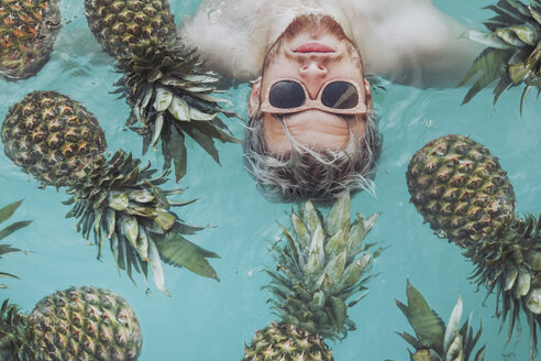 Young man in swiming pool surrounded by pineapples - RTBF00747