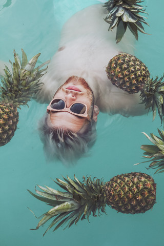 Junger Mann im Schwimmbad, umgeben von Ananas, lizenzfreies Stockfoto