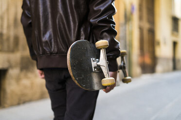 Young man carrying skateboard in the city - KKAF00500