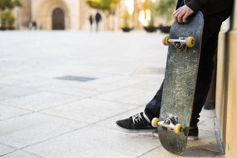 Junger Mann mit Skateboard lehnt an Hausfassade, lizenzfreies Stockfoto