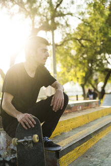 Junger Mann sitzt mit Skateboard in einem Skatepark - KKAF00514