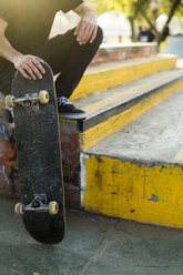 Man sitting with skateboard in a skatepark - KKAF00515