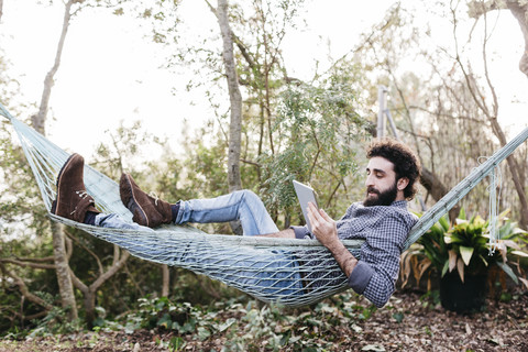 Mann in Hängematte liegend mit Tablet, lizenzfreies Stockfoto