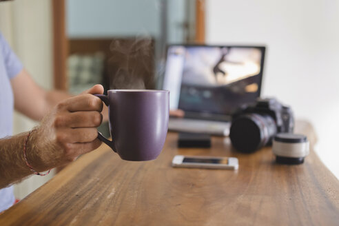 Fotograf hält Kaffeetasse am Schreibtisch zu Hause - KNTF00776