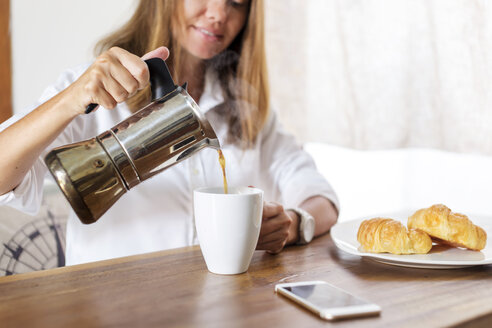 Woman at breakfast table pouring coffee into cup - KNTF00777