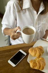 Woman at breakfast table with coffee, croissants and cell phone - KNTF00783