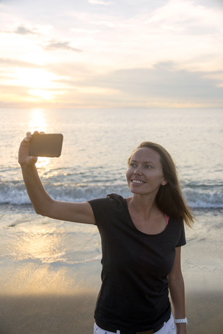 Indonesia, Bali, woman taking a selfie on the beach at sunset stock photo