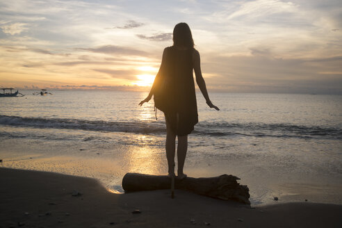 Indonesien, Bali, Frau beobachtet den Sonnenuntergang über dem Meer - KNTF00803