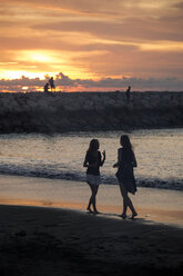 Indonesien, Bali, zwei Frauen gehen bei Sonnenuntergang am Strand spazieren - KNTF00807
