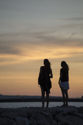 Indonesien, Bali, zwei Frauen beobachten den Sonnenuntergang über dem Meer - KNTF00809