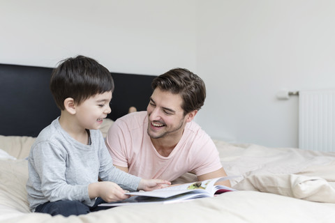 Happy father and son reading a book in bed stock photo