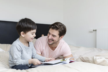 Happy father and son reading a book in bed - SHKF00736