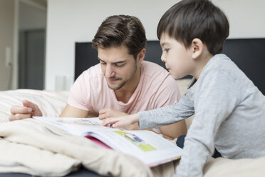 Father and son reading a book in bed - SHKF00737