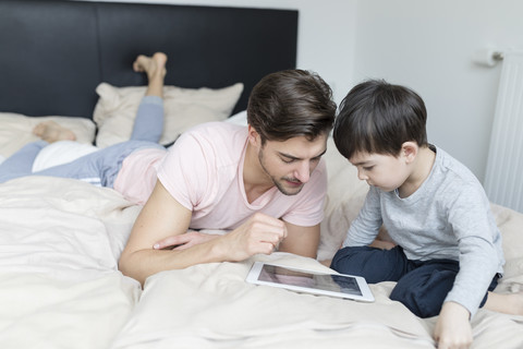 Father and son looking at tablet in bed stock photo