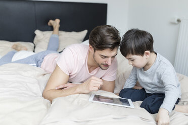 Father and son looking at tablet in bed - SHKF00738