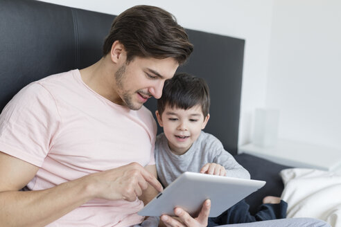 Vater und Sohn schauen auf ein Tablet im Bett - SHKF00739