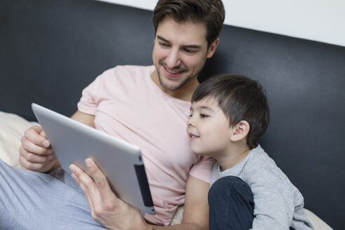 Vater und Sohn schauen auf ein Tablet im Bett - SHKF00740