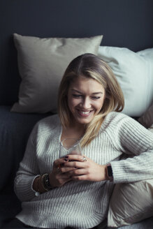 Smiling blond woman with glass of coffee relaxing on couch at home - NAF00062