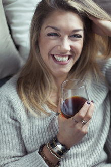 Portrait of laughing blond woman with glass of coffee relaxing on couch at home - NAF00065