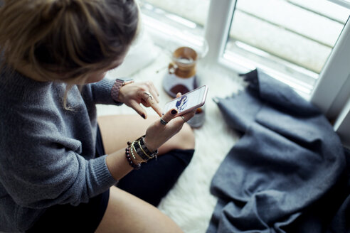 Young woman relaxing on sheepskin at home using cell phone - NAF00072