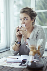 Porträt einer jungen Frau mit einem Glas Kaffee, die durch ein Fenster schaut - NAF00080