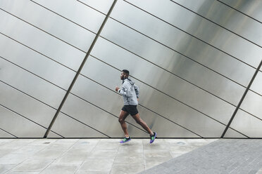 Young man running along building front - BOYF00670