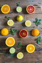 Geschnittene und ganze Zitronen, Orangen und Limetten sowie Minzblätter auf Holz - GIOF02241