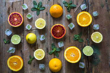Sliced and whole lemons, oranges and limes, mint leaves and ice cubes on wood - GIOF02242