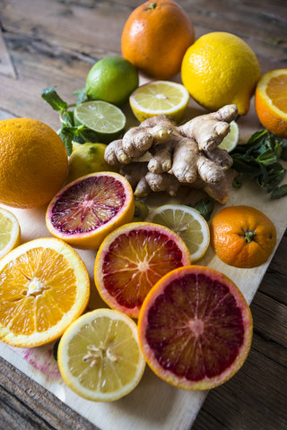 Sliced and whole lemons, oranges and limes, ginger root and mint leaves on wooden board stock photo