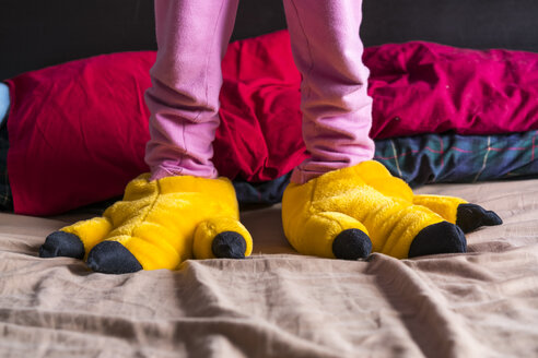Girl standing on bed wearing yellow fun slippers - XCF00149