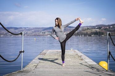 Frau übt Yoga auf einem Pier an einem See - SIPF01468