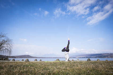 Frau übt Yoga und macht einen Kopfstand an einem See, lizenzfreies Stockfoto