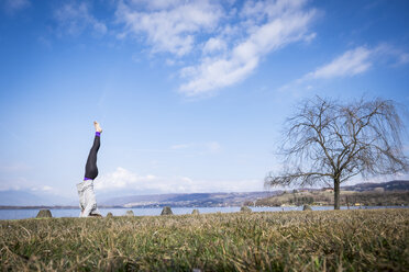 Frau übt Yoga und macht einen Kopfstand an einem See - SIPF01471