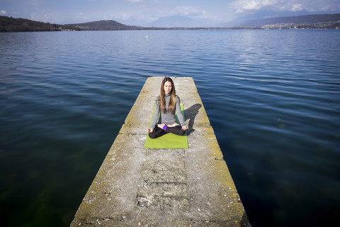 Frau übt Yoga auf einem Pier an einem See, lizenzfreies Stockfoto