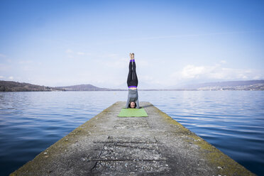 Woman practicing yoga doing a headstand on a pier at a lake - SIPF01473