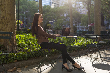 USA, New York, Manhattan, young businesswoman with laptop sitting at table in a park - BOYF00691