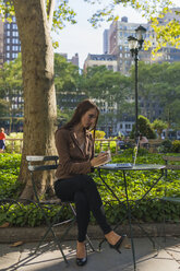 USA, New York, Manhattan, junge Geschäftsfrau mit Laptop sitzt an einem Tisch in einem Park und macht sich Notizen - BOYF00694