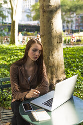 USA, New York, Manhattan, nachdenkliche junge Geschäftsfrau sitzt mit Laptop an einem Tisch in einem Park - BOYF00695