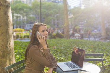 USA, New York, Manhattan, junge Geschäftsfrau beim Telefonieren an einem Tisch in einem Park - BOYF00697