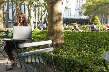 USA, New York, Manhattan, junge Geschäftsfrau telefoniert an einem Tisch in einem Park mit Laptop - BOYF00698