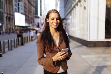 USA, New York, Manhattan, lächelnde junge Geschäftsfrau, die auf ihr Mobiltelefon schaut - BOYF00719