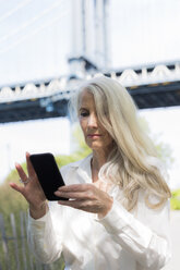 USA, Brooklyn, reife Frau benutzt Handy vor der Manhattan Bridge - GIOF02288