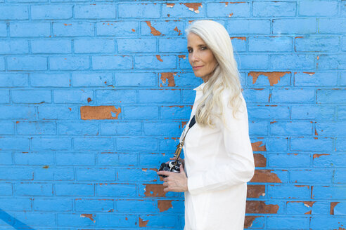 Porträt einer reifen Frau mit Kamera vor einer blauen Wand - GIOF02303
