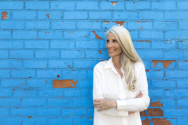 Smiling mature woman standing in front of light blue wall - GIOF02305