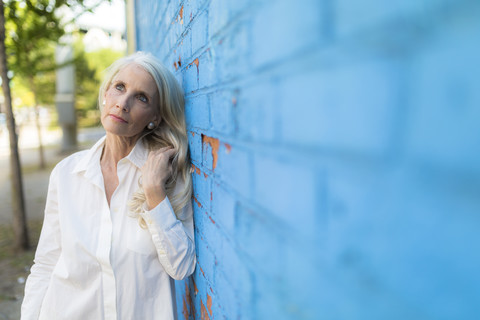 Porträt einer träumenden reifen Frau, die sich an eine hellblaue Wand lehnt, lizenzfreies Stockfoto
